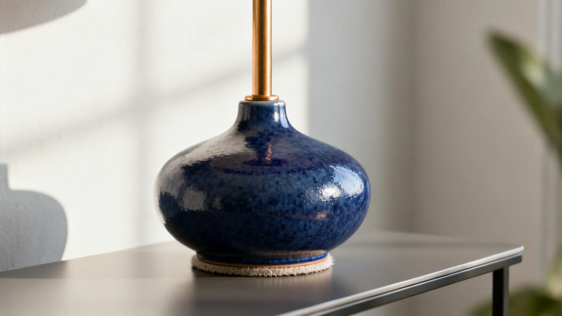 Navy glazed ceramic lamp with warm brass neck on a narrow side table