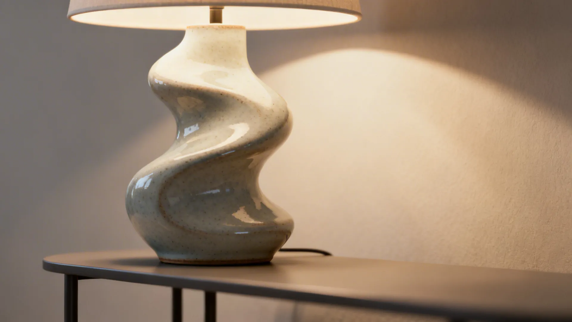 Close-up of a curvy ceramic sculptural table lamp with warm light and glossy glaze.