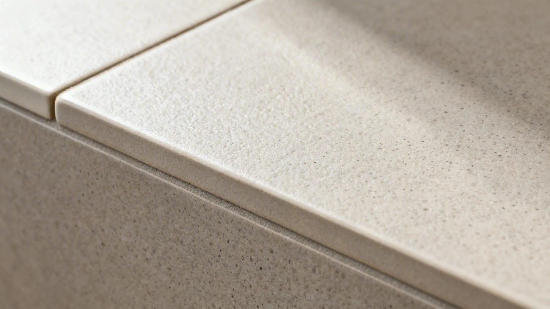 Macro of matte textured ceramic tile with eased edge and matching grout.