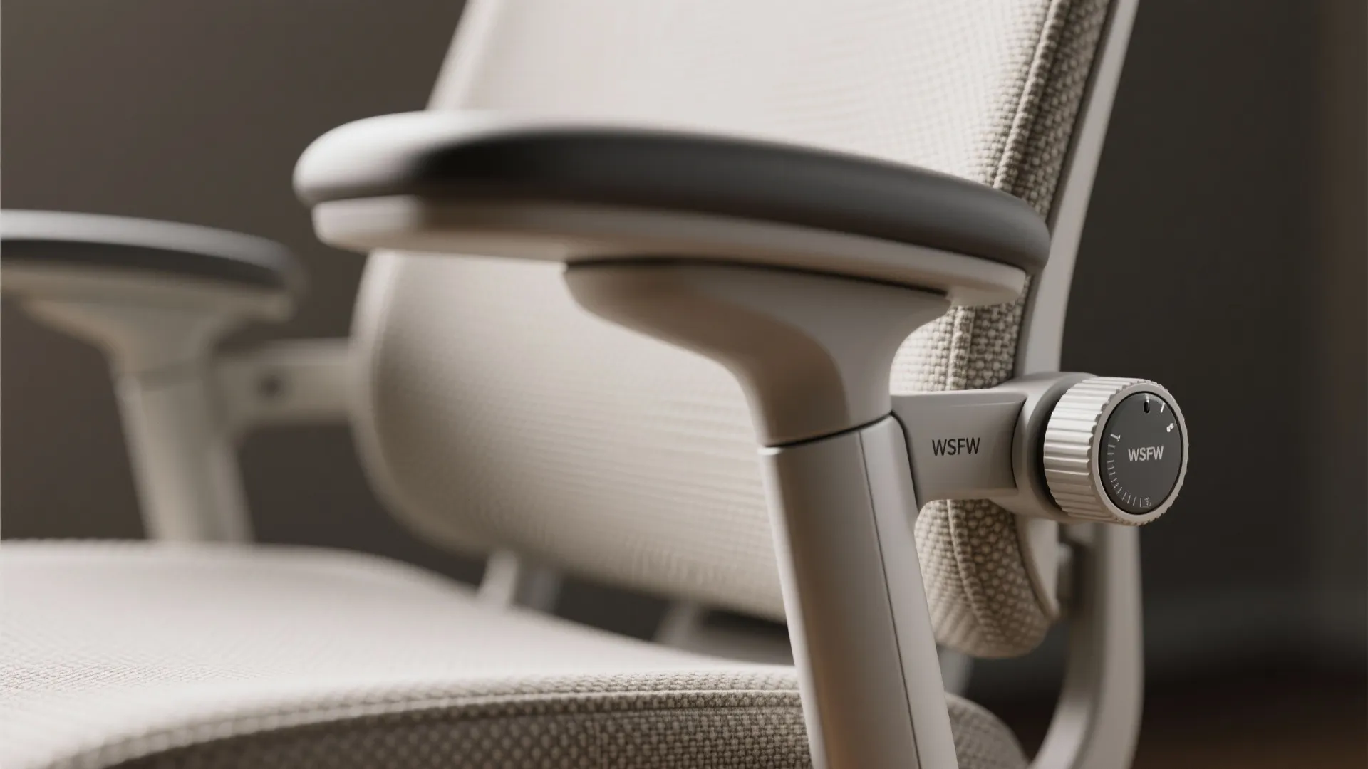 Close up of an ergonomic office chair armrest with adjustable dial and light grey mesh fabric