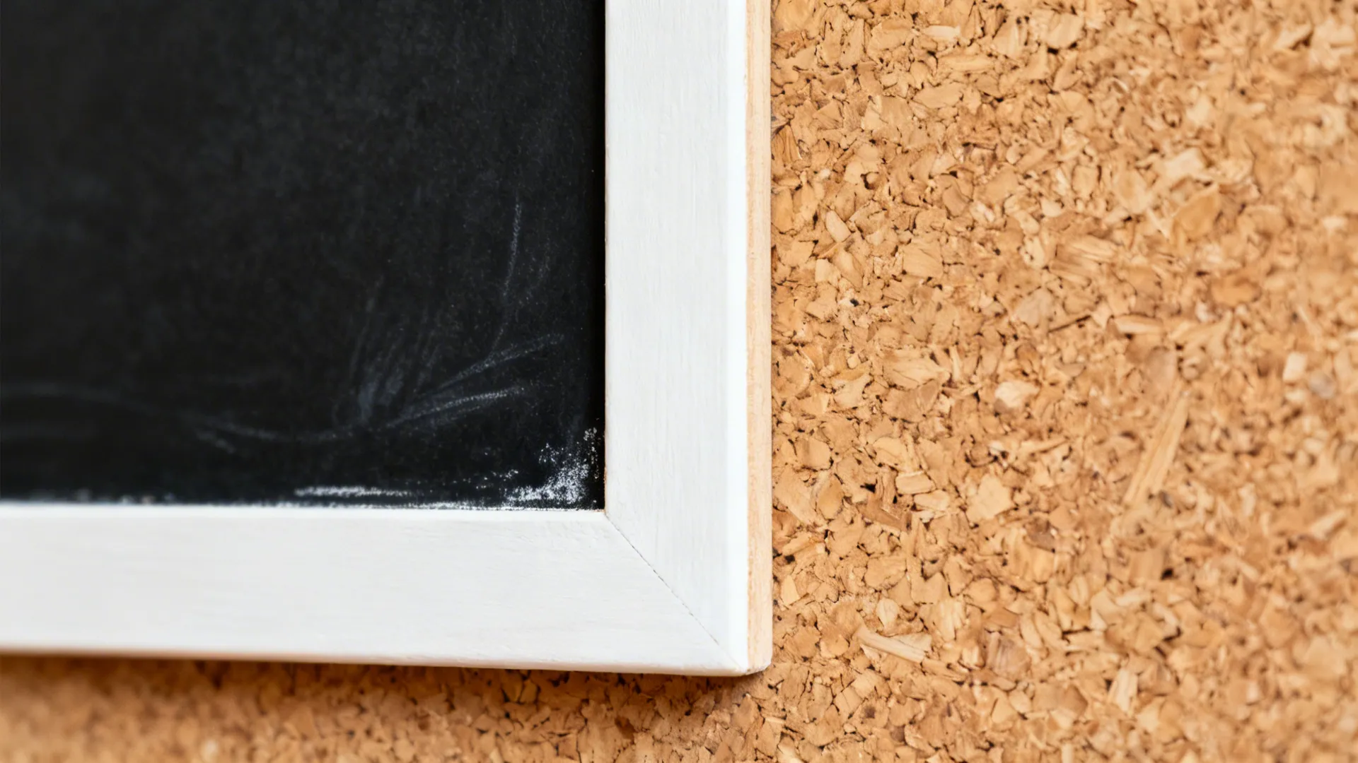 Macro showing cork texture and matte chalkboard frame with faint chalk marks.