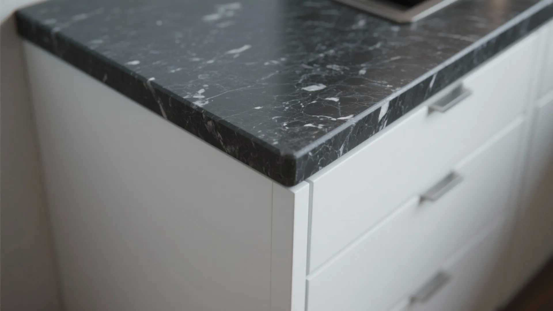 Close-up of charcoal quartz countertop edge meeting matte white cabinet, showing stone texture and contrast.