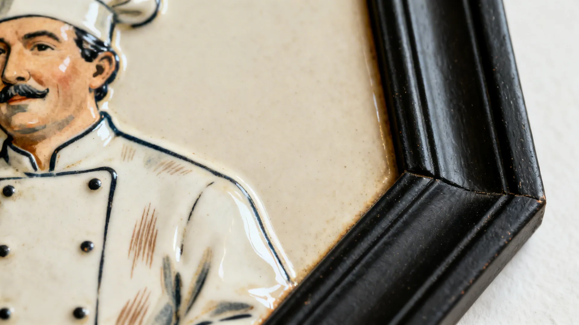 Macro view of a vintage chef plaque enamel and a matte black frame corner with fine texture.
