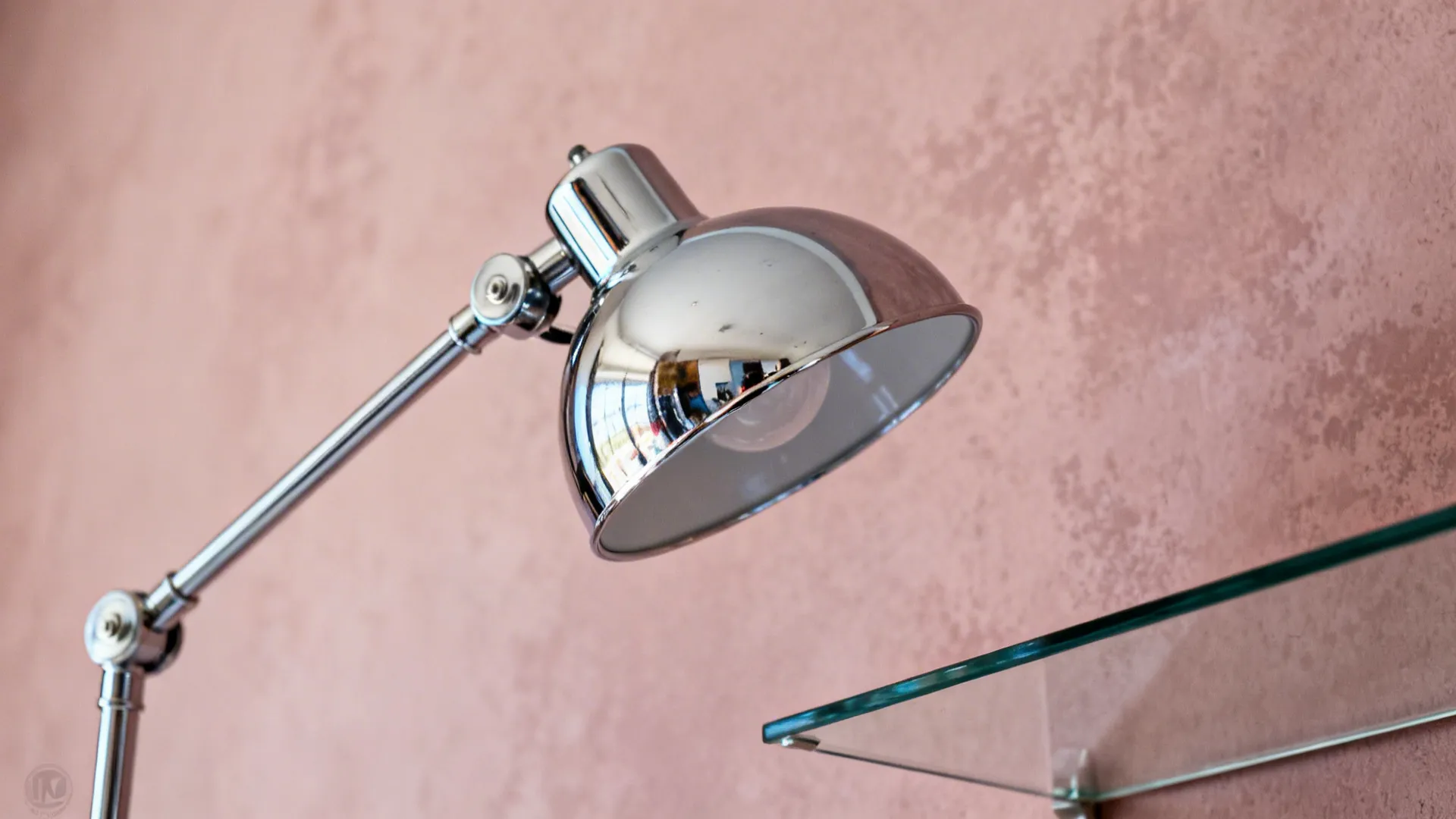 Close-up of chrome lamp and glass shelf against a dusty-rose wall.