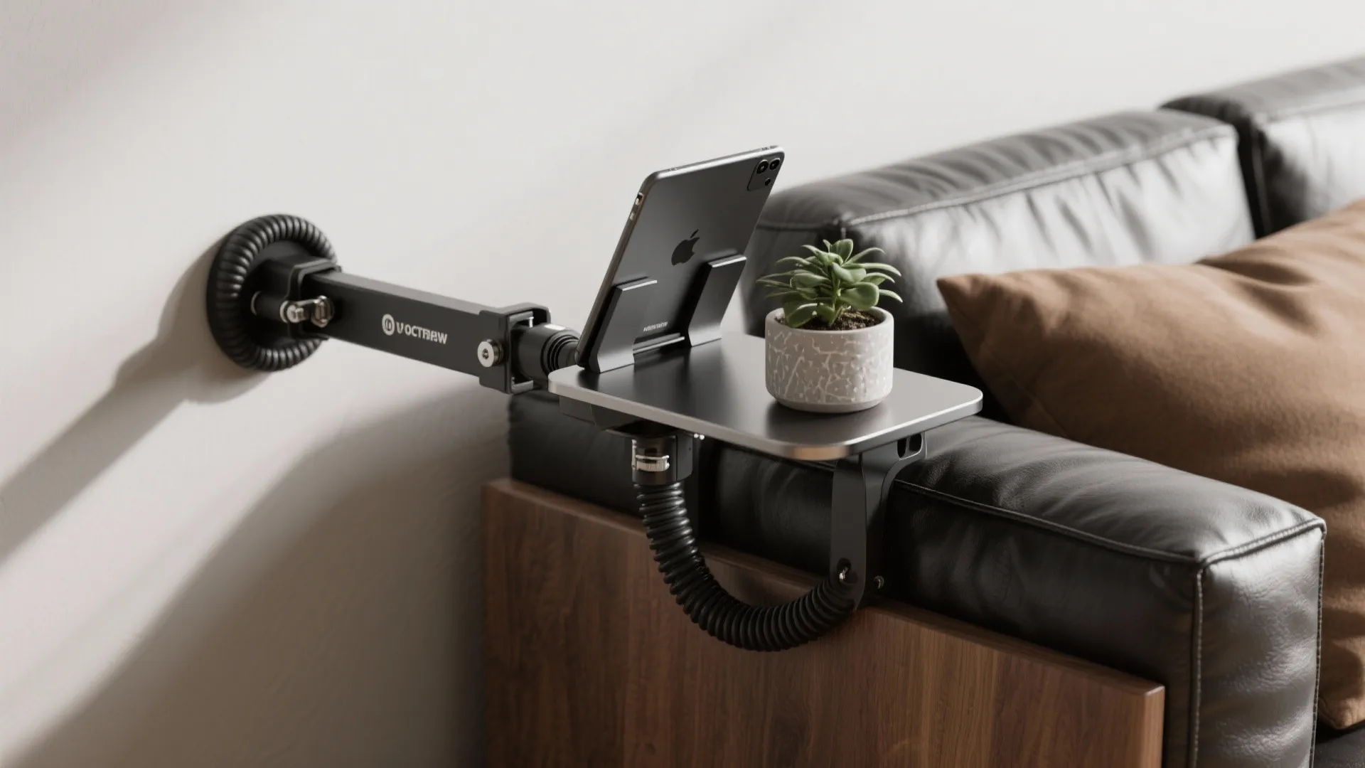 Rubber-lined metal clamp-on platform attached to a faux-leather sofa arm holding a tablet and small plant.