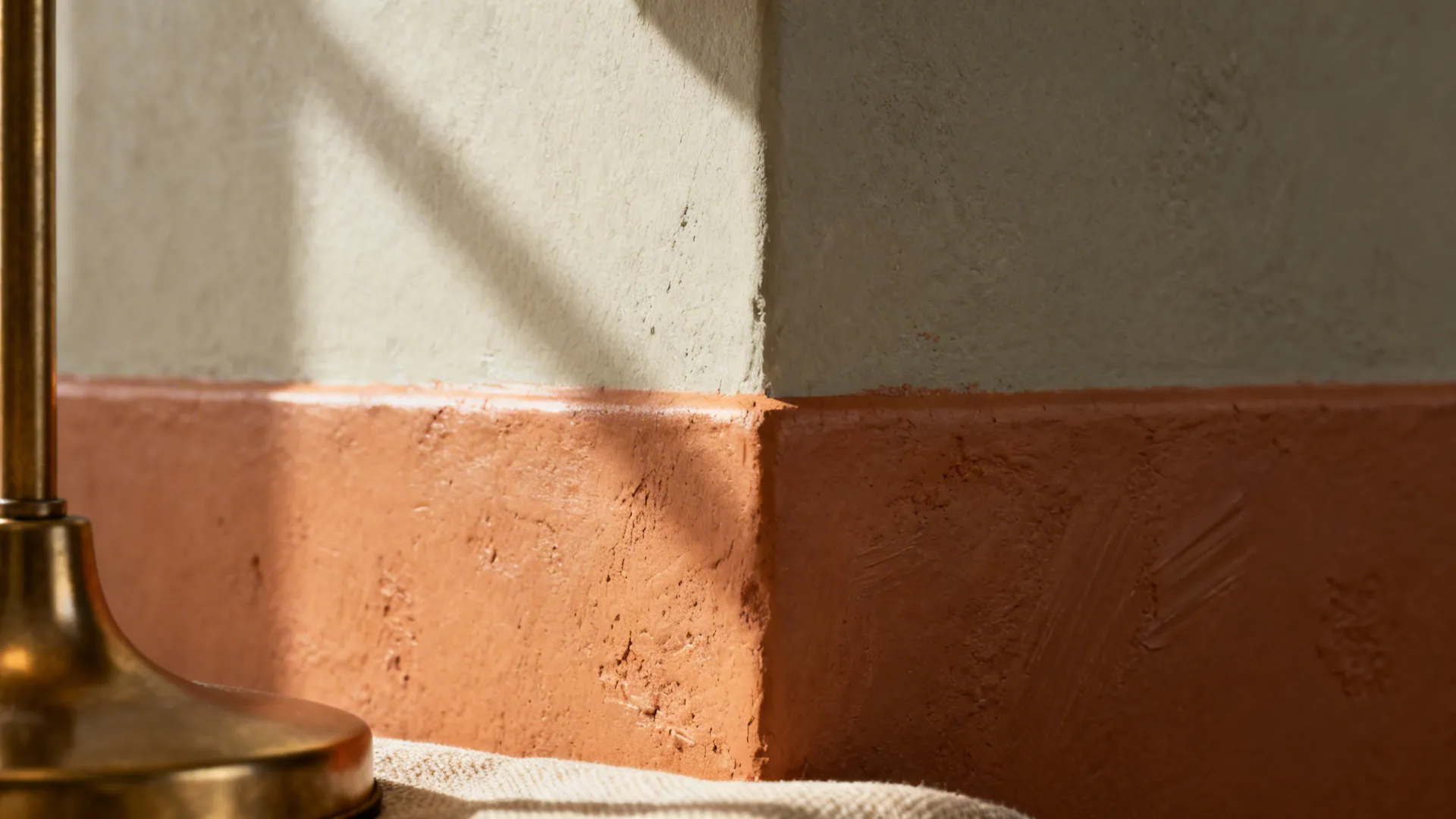 Close-up of matte terracotta paint meeting greige wall with subtle texture and brass accent.