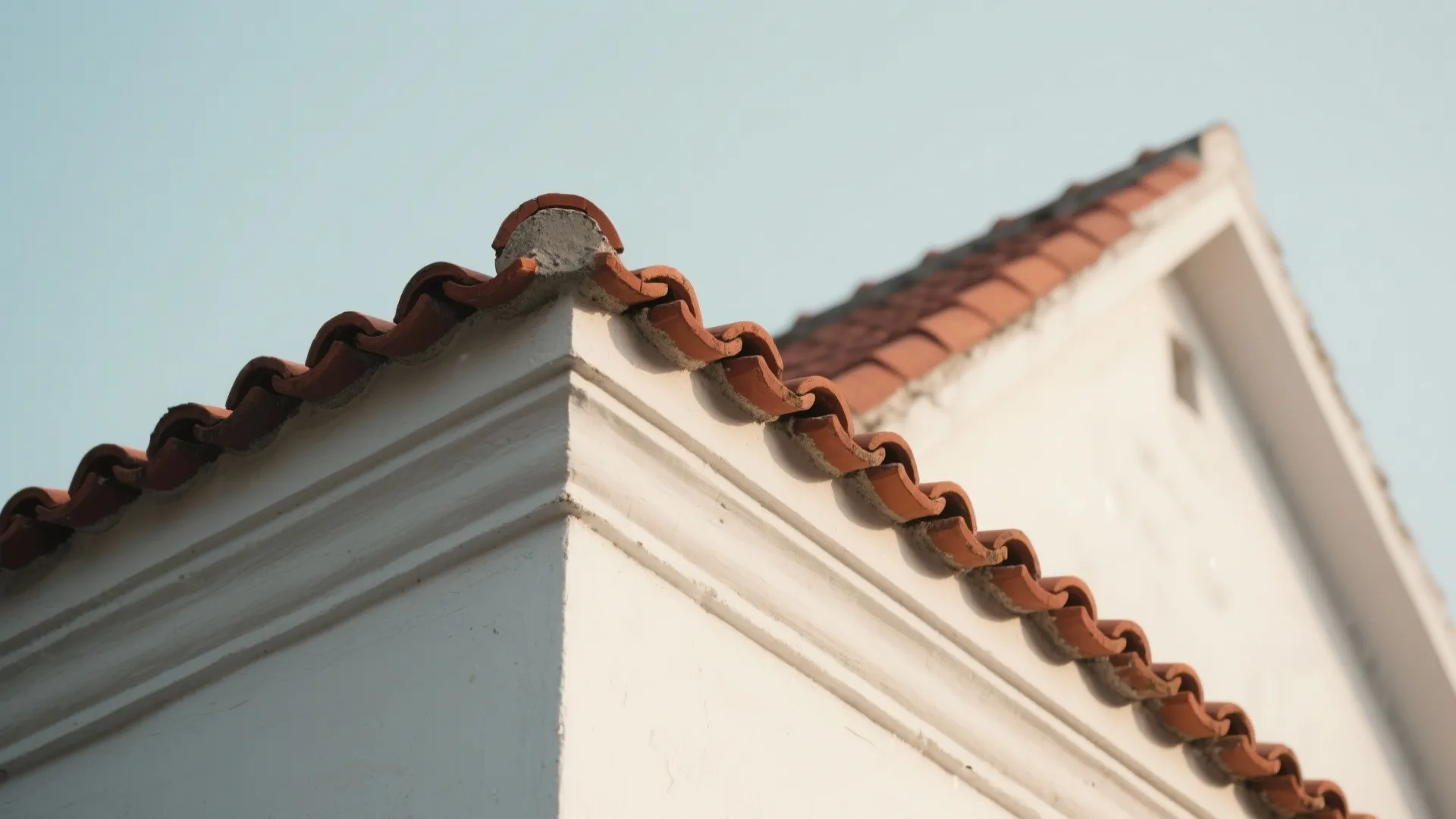 Close up view of red clay roof tiles on a white wall with blue sky