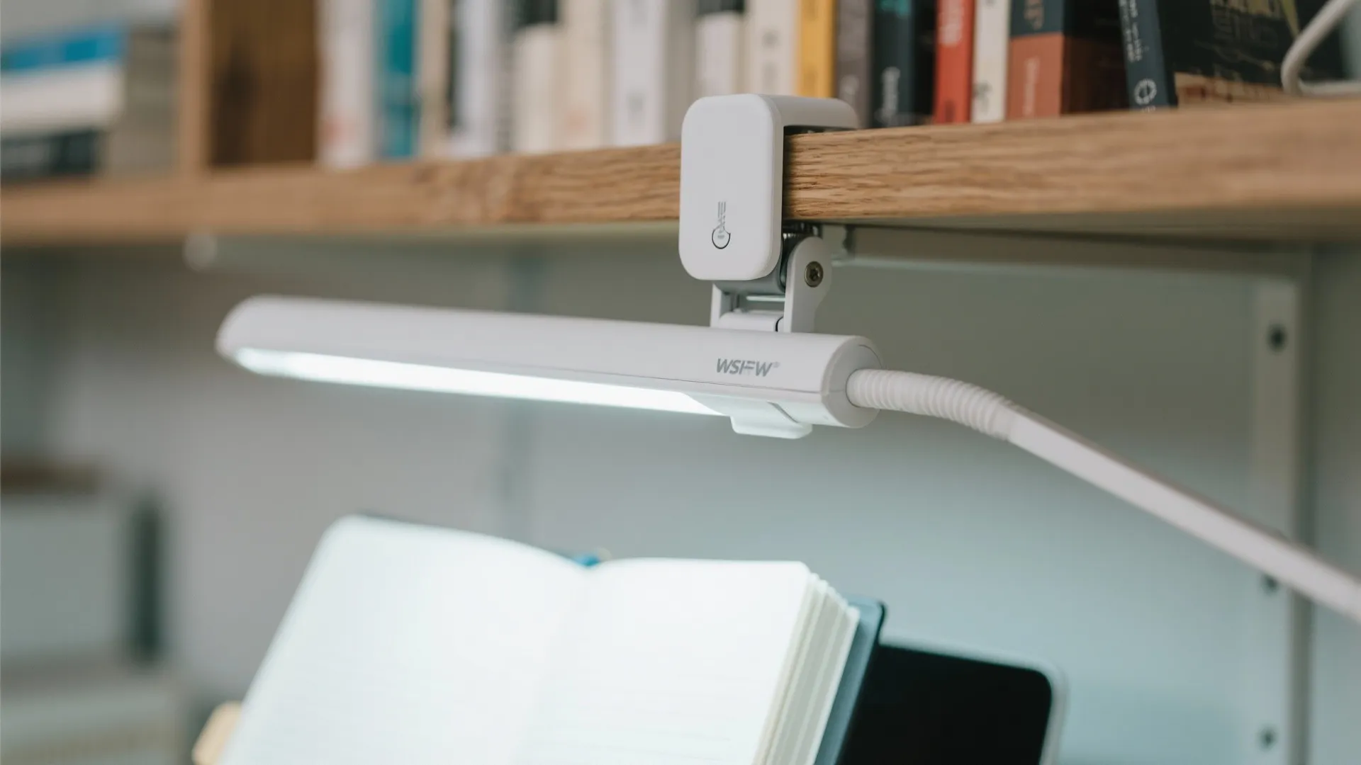 White clip on light fixture attached to wooden shelf above an open notebook and books