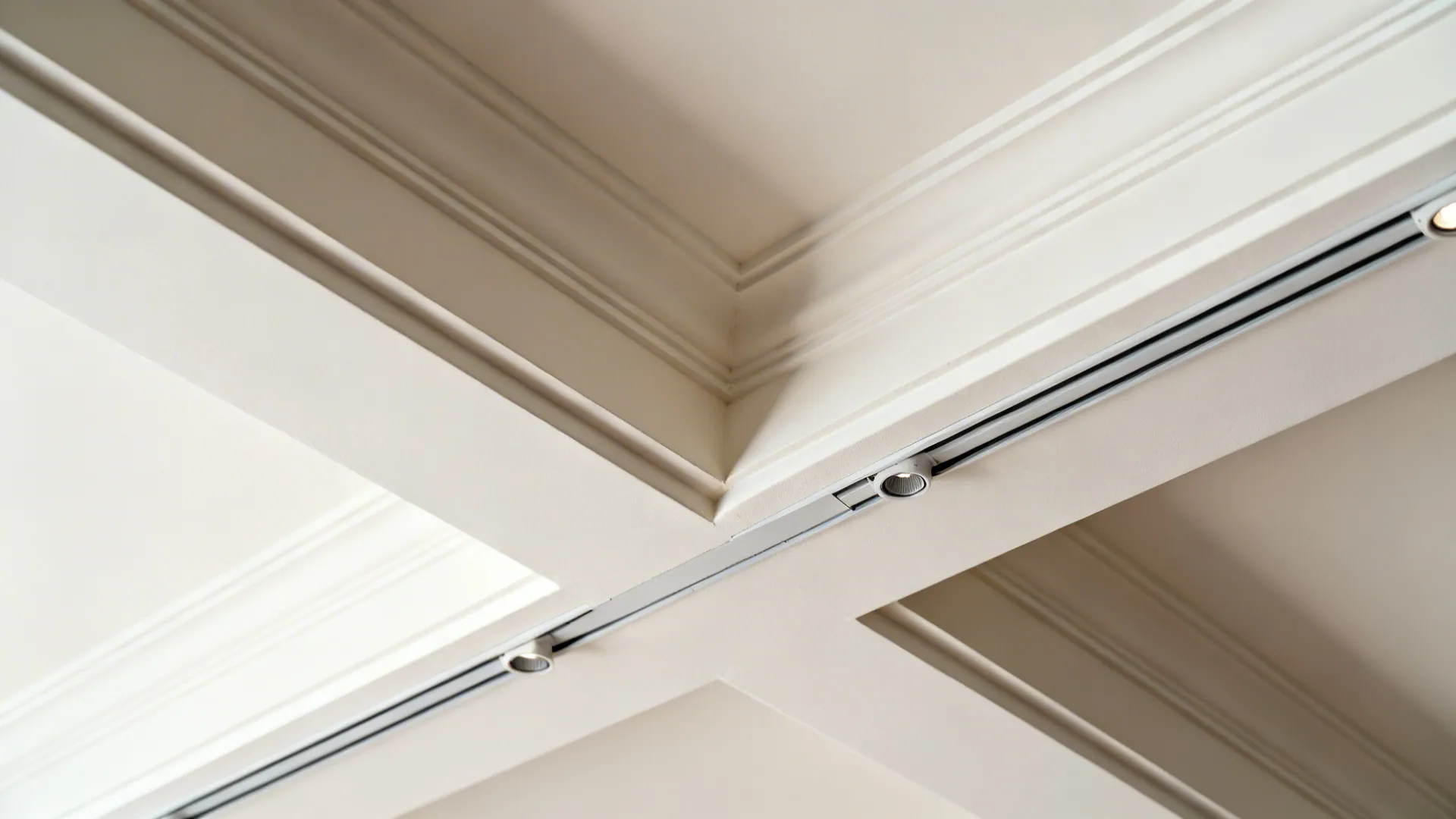 Close up of a white ceiling with decorative trim and small modern track light fixture