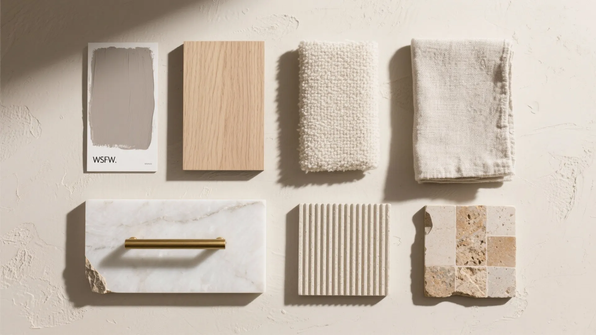 Flat lay of greige paint, ash veneer, brushed brass, linen, quartz, and stone swatches in warm light
