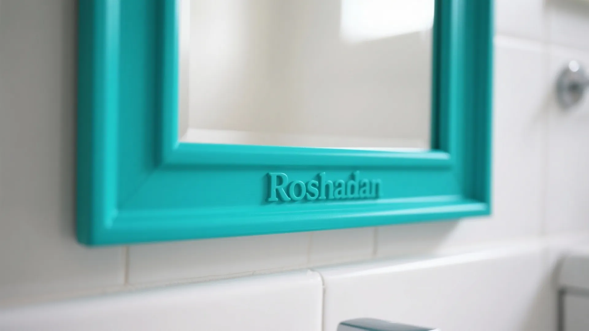 Close up of a bright teal mirror frame with brand name text on white bathroom tiles