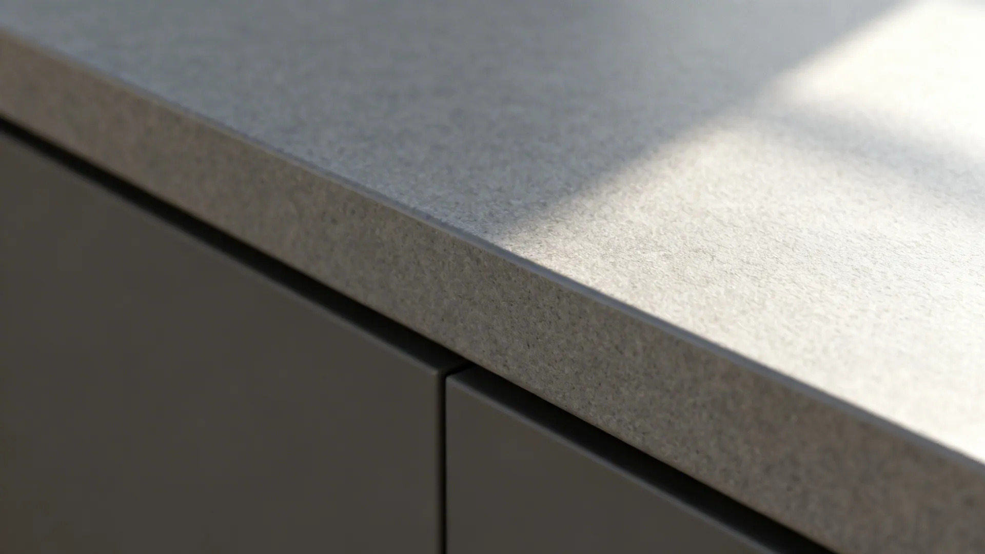 Close up of grey stone countertop edge with smooth finish and grey cabinet drawer below