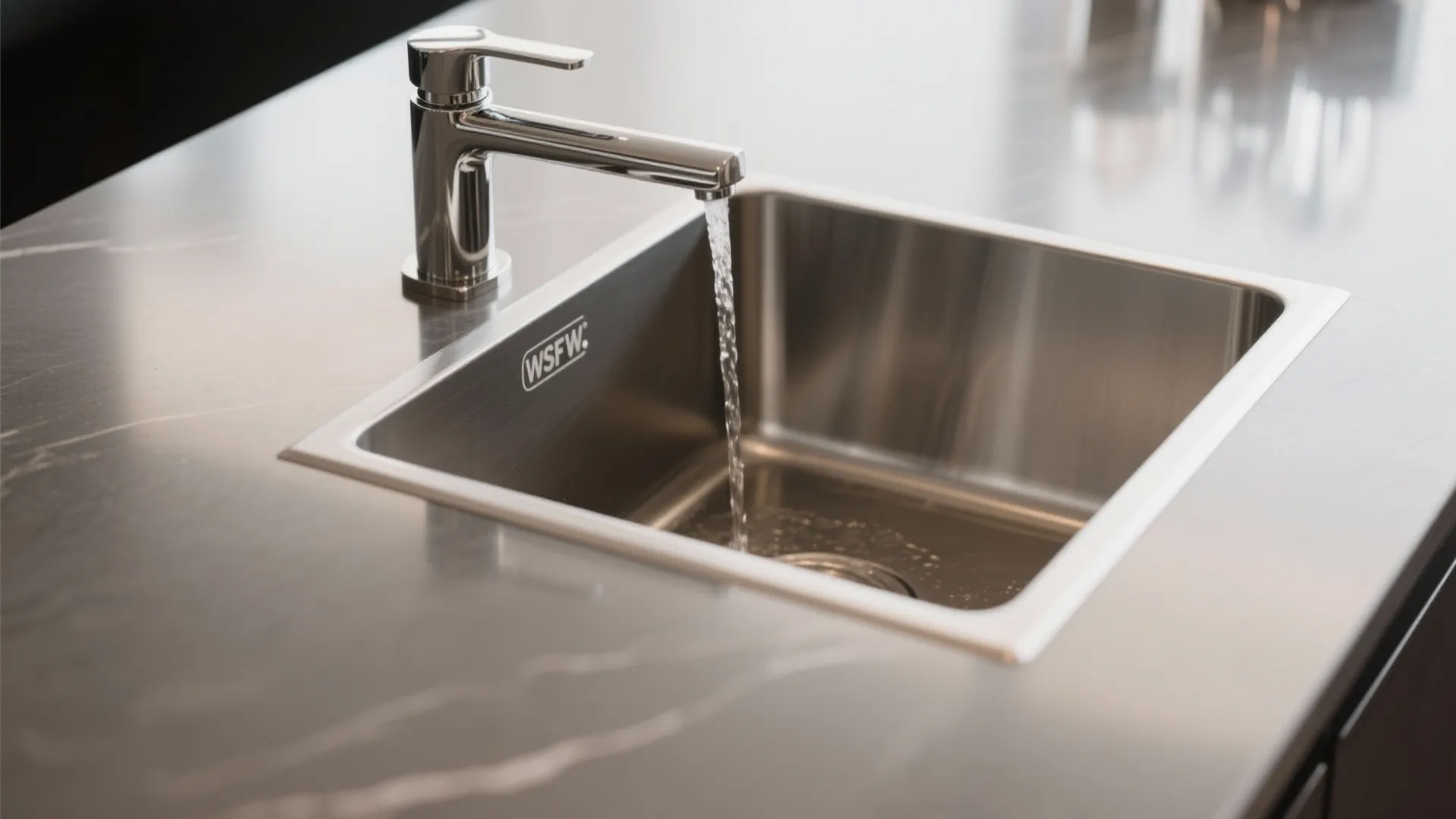 Stainless steel kitchen sink with water flowing from a silver faucet onto a dark countertop