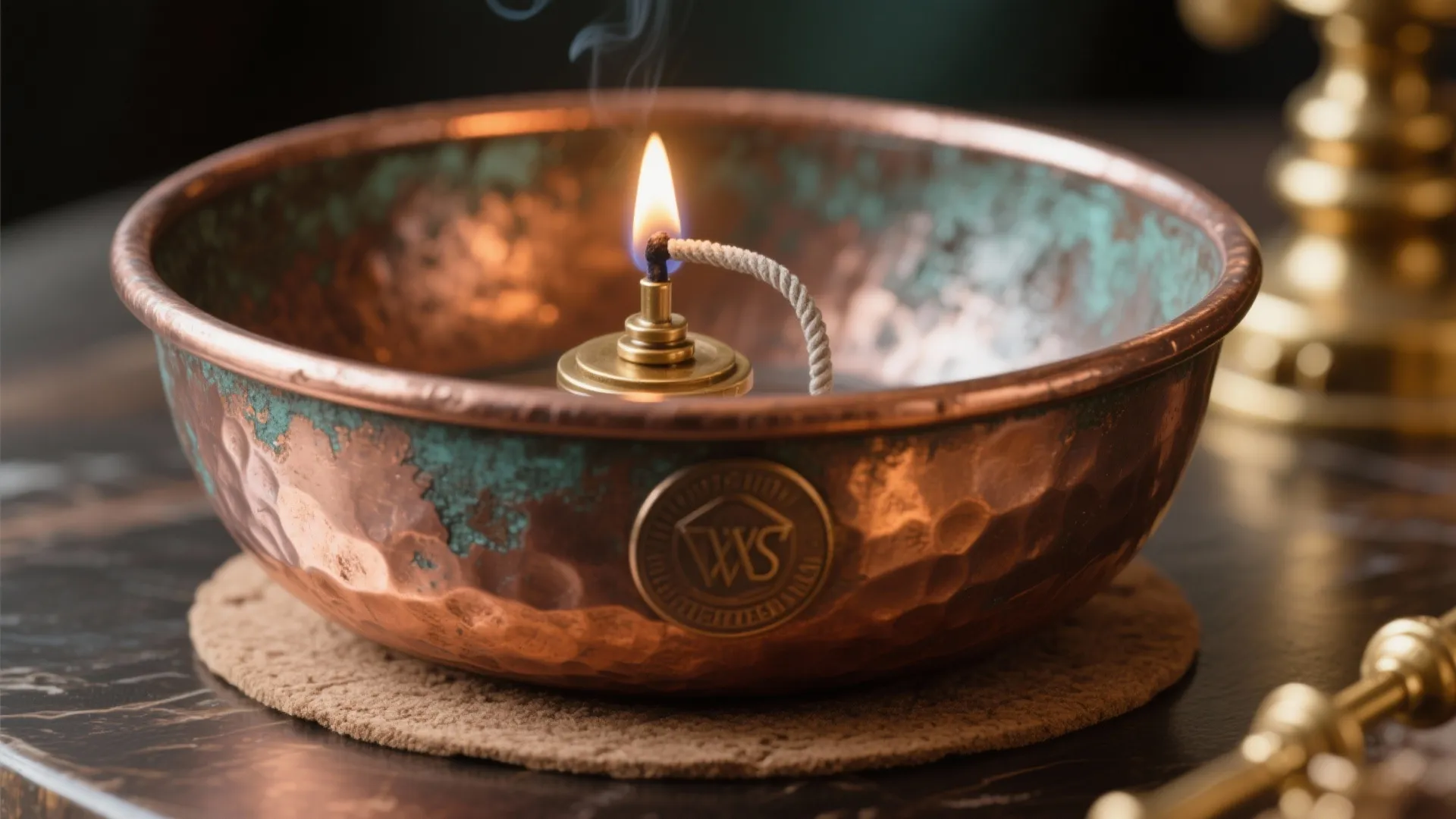 Hammered copper bowl with small burning flame, oil lamp wick, and green patina on table