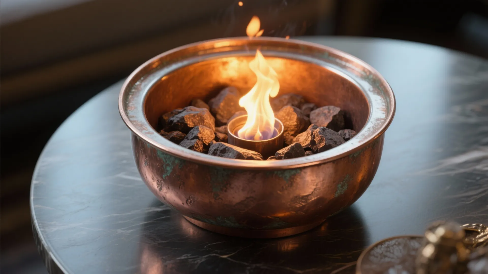 Round copper fire bowl filled with dark stones and a central flame on dark marble table