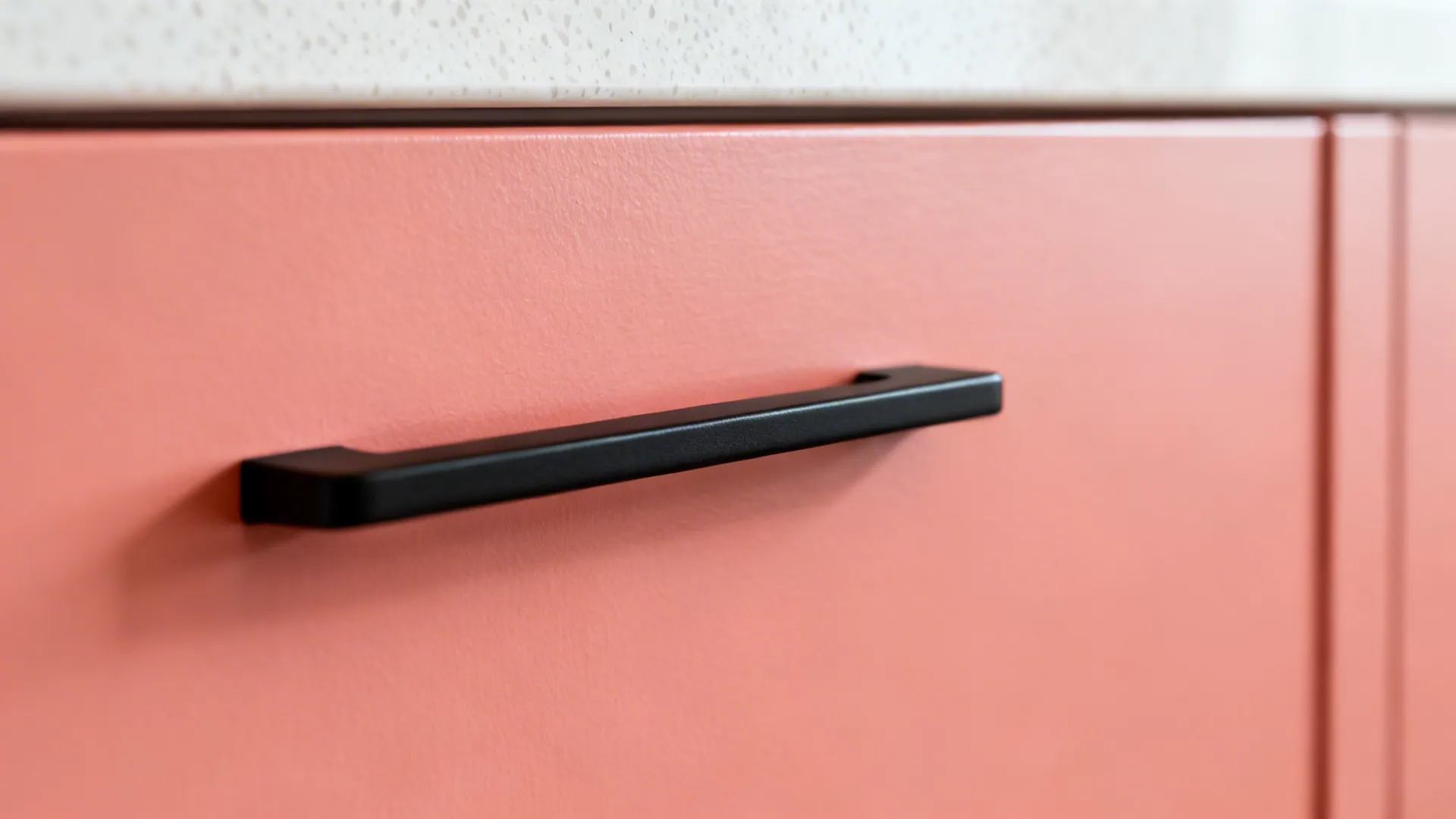 Macro of coral cabinet with matte black bar pull showing crisp textures.