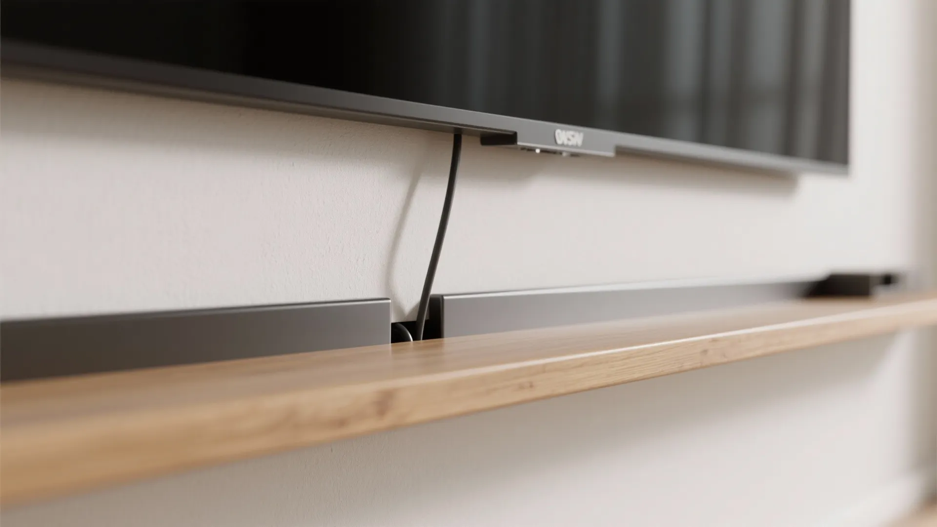 Macro of a sleek cord channel and floating media shelf beneath a wall-mounted TV.