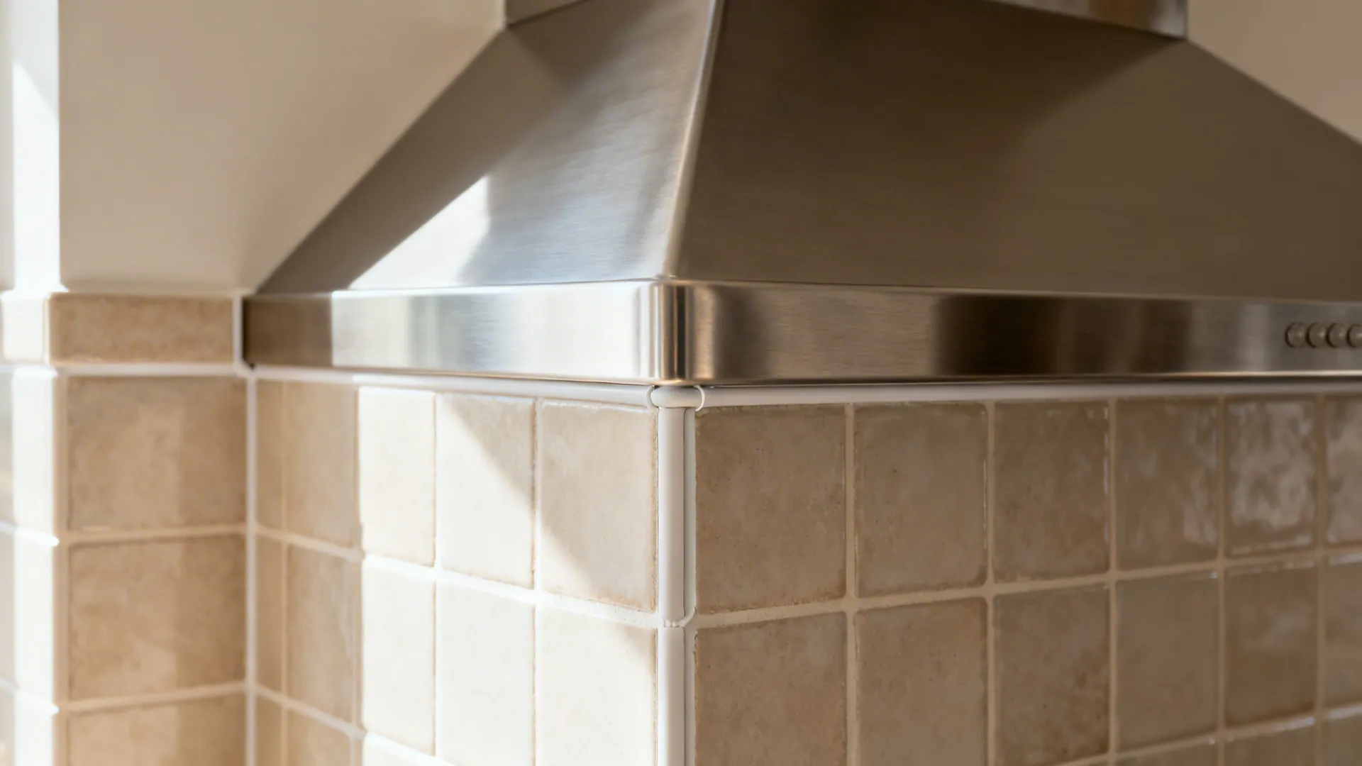 Close-up of a corner chimney hood edge and neatly finished tiled backsplash junction.