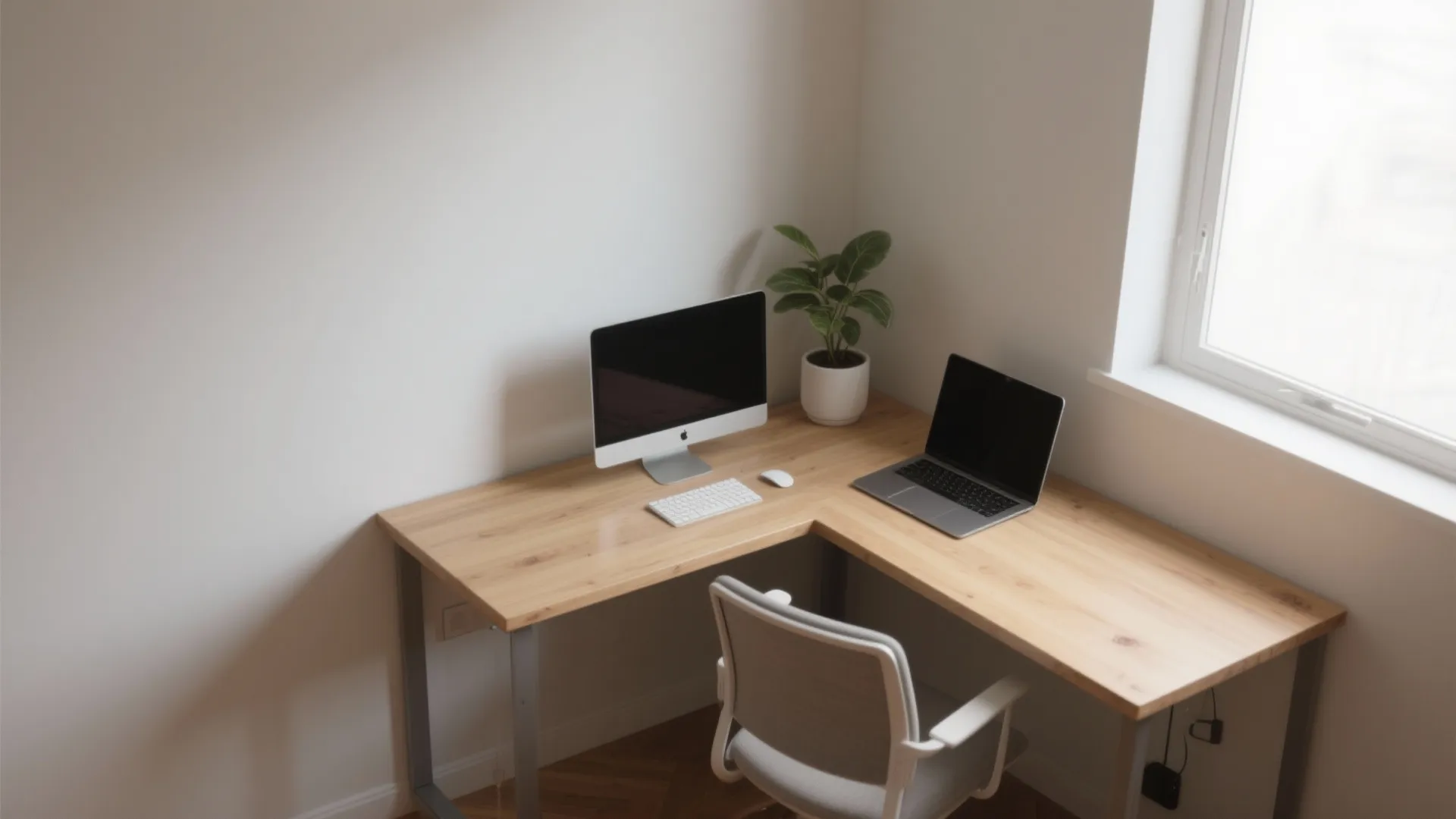 Modern wooden corner L-shaped desk with a computer monitor laptop plant and grey office chair