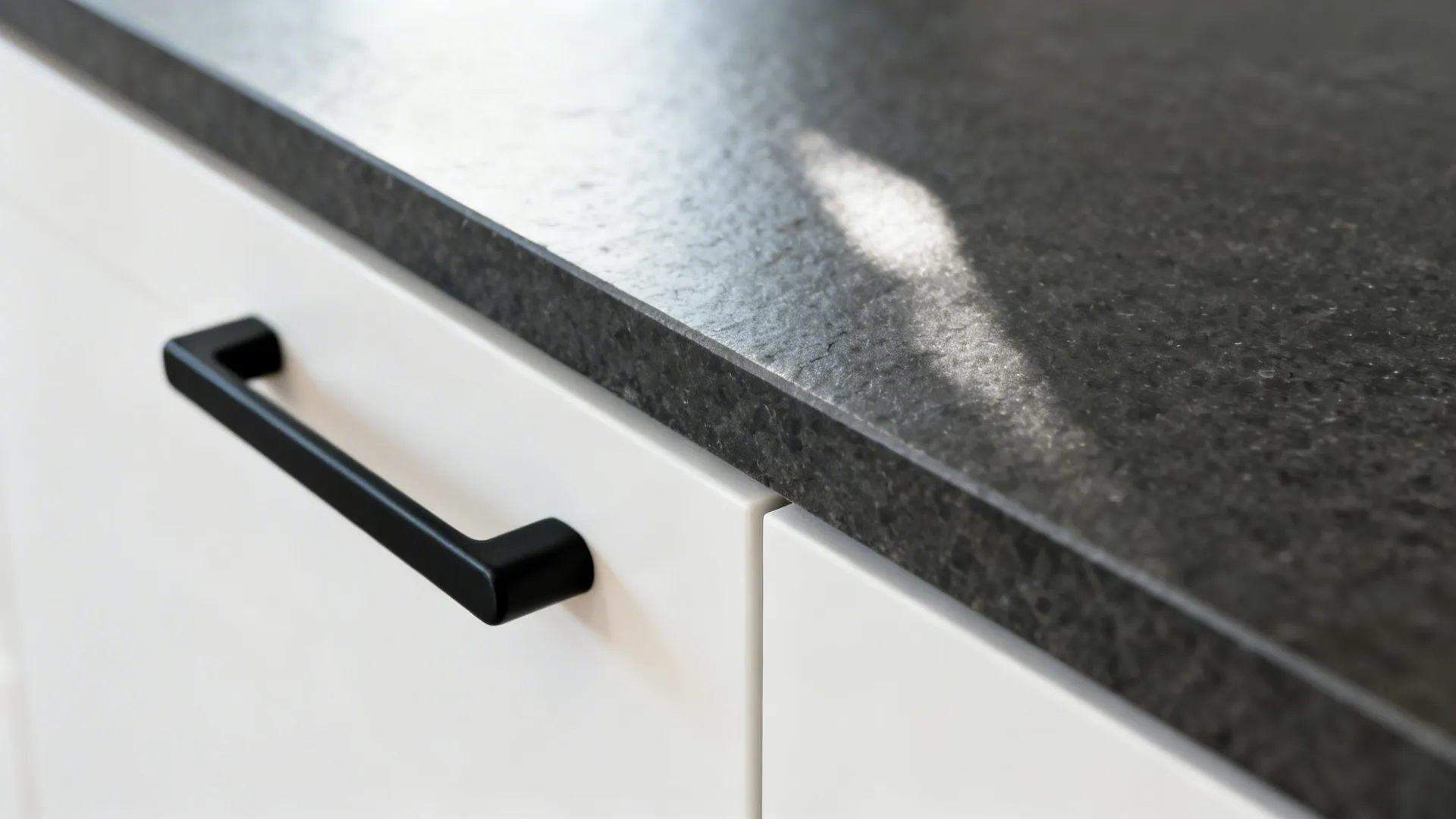 Close-up of dark honed counter edge with matte black pull on a white cabinet.