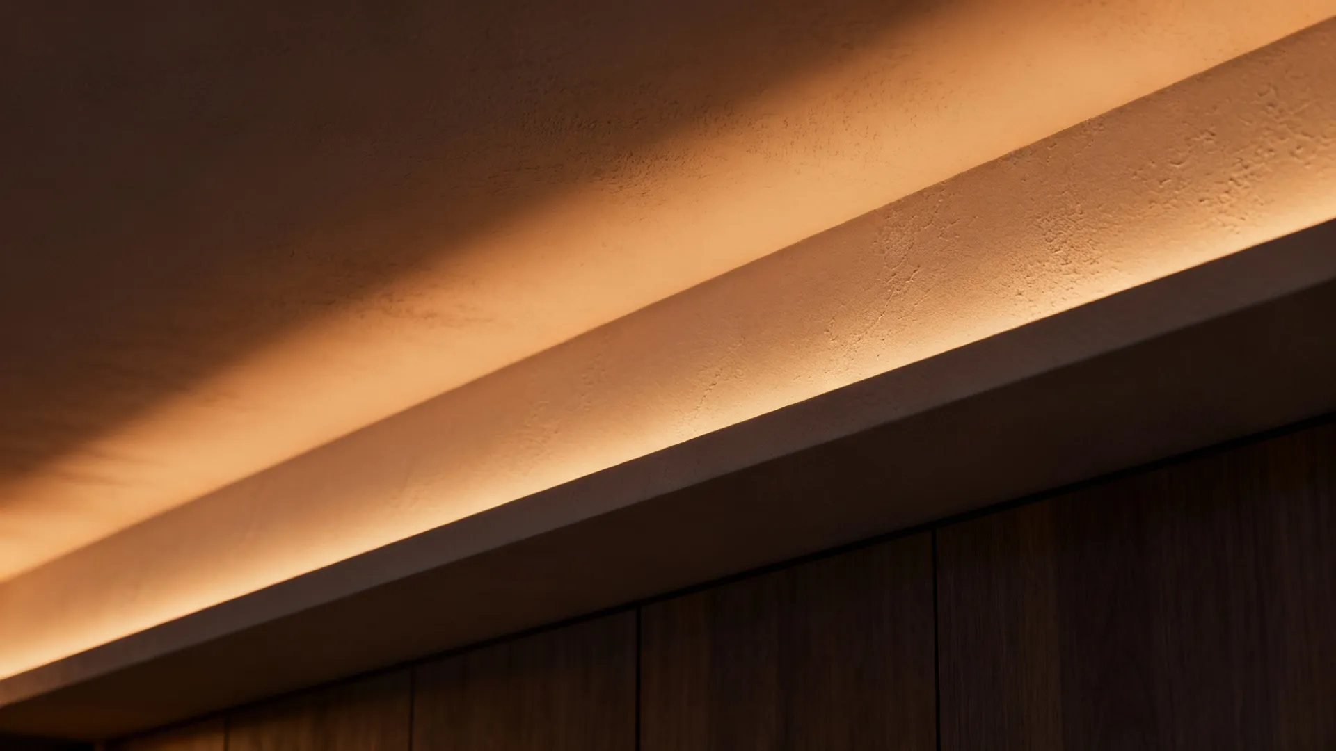 Close up of warm hidden light fixture glowing from a recessed ceiling above dark wooden cabinets