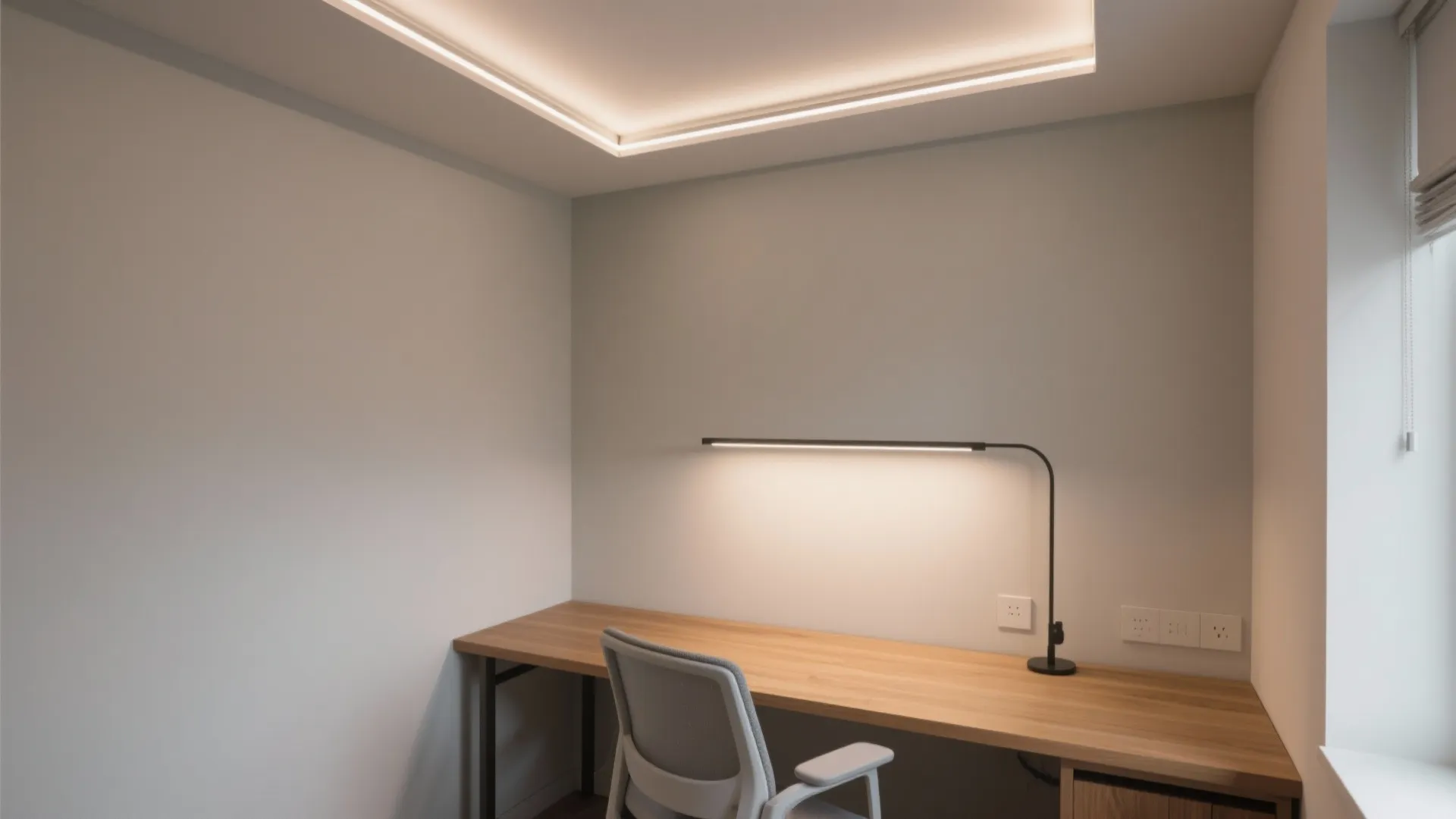 Minimalist home office with wooden desk, grey chair, black lamp, and warm recessed ceiling lights