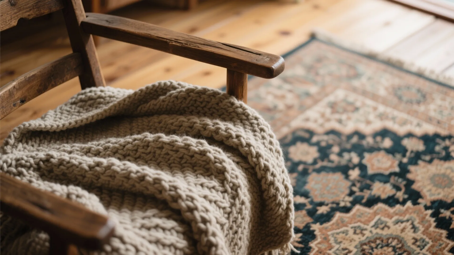 Close up of a thick knit blanket on a wooden chair with a patterned floor rug