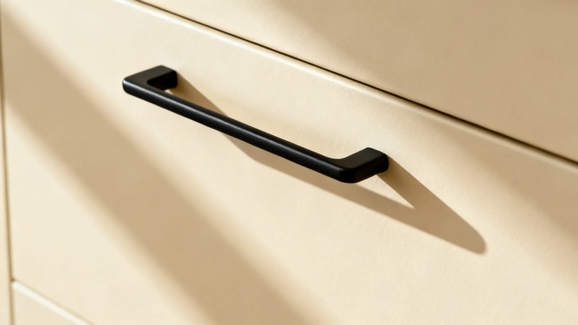 Macro detail of matte cream cabinet door with a slim black pull handle.