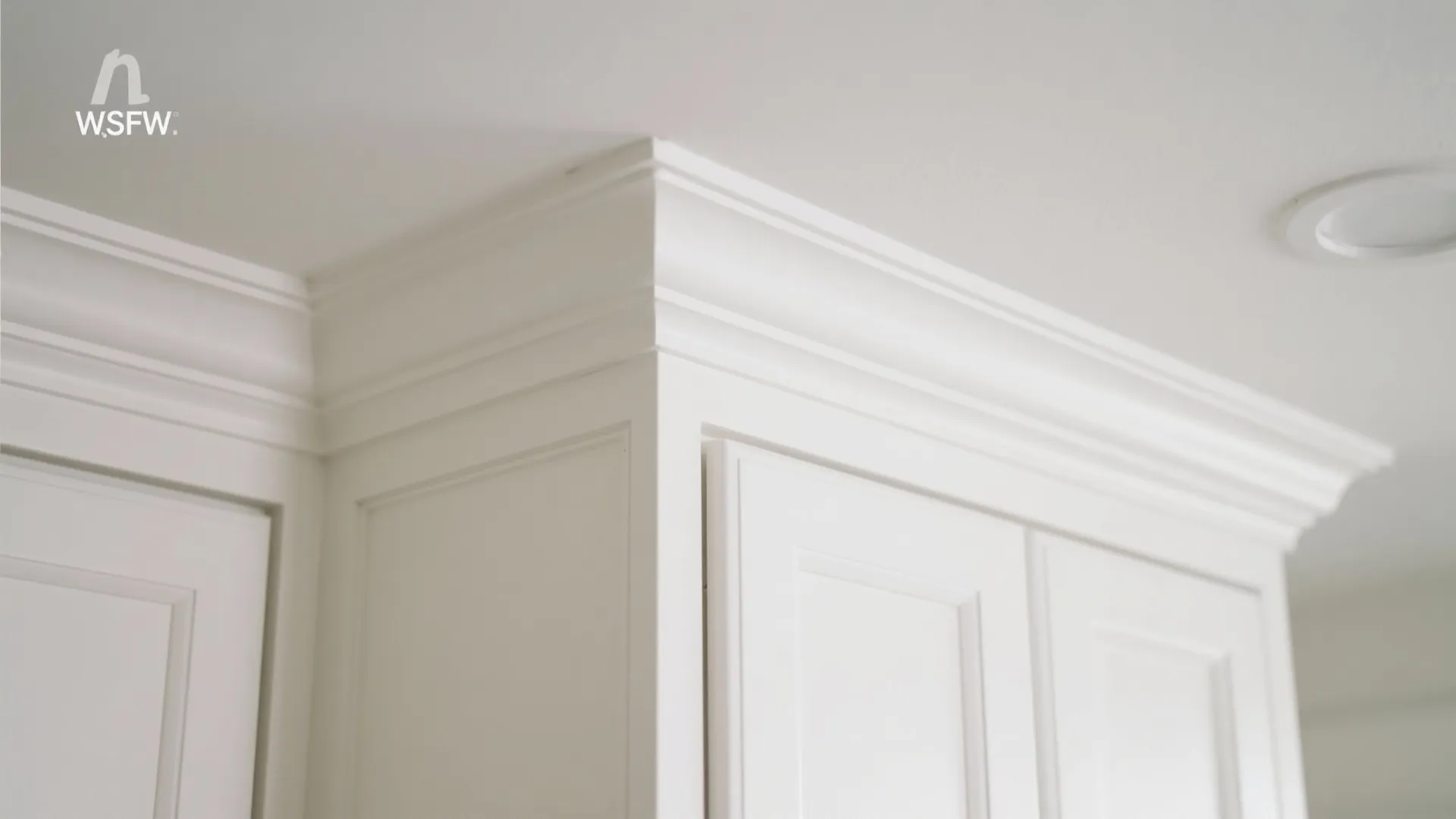Detailed view of white decorative trim on top of white kitchen cabinets near the ceiling