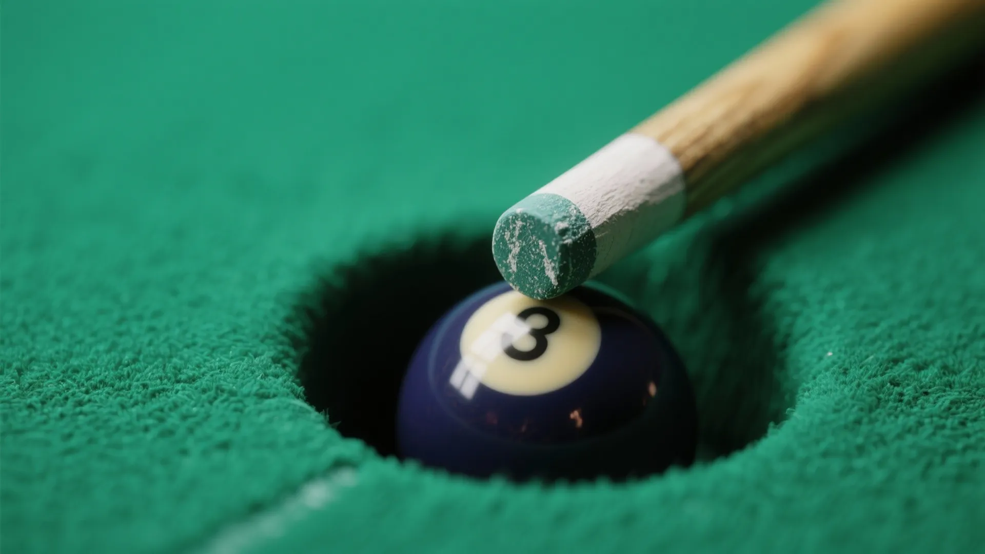 Close up of a wooden pool cue stick hitting a blue ball into a hole