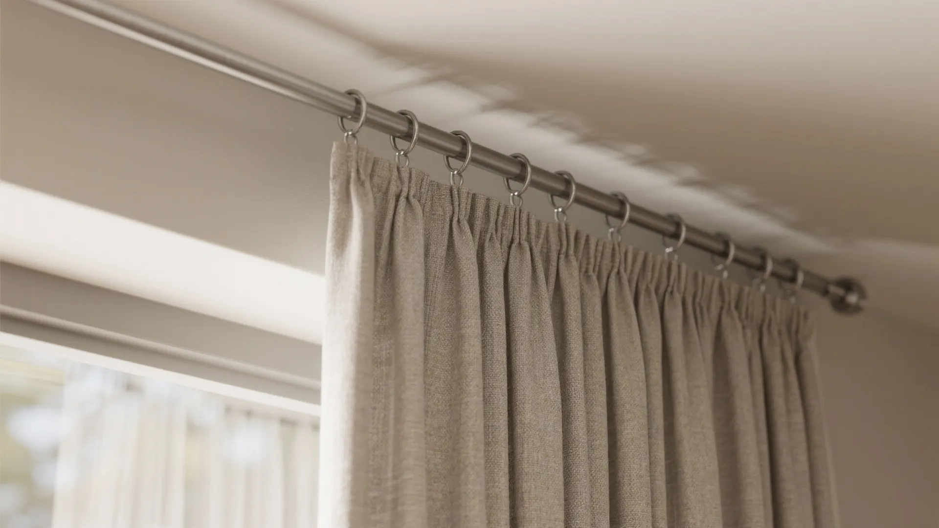 Close up view of beige curtain fabric hanging from a metal rod with small rings