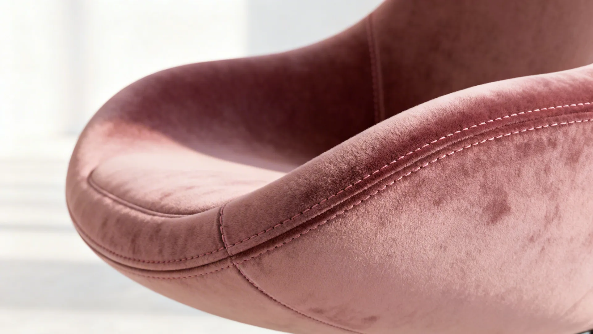 Macro view of a curved dusty-rose velvet chair showing plush short-pile texture and stitching