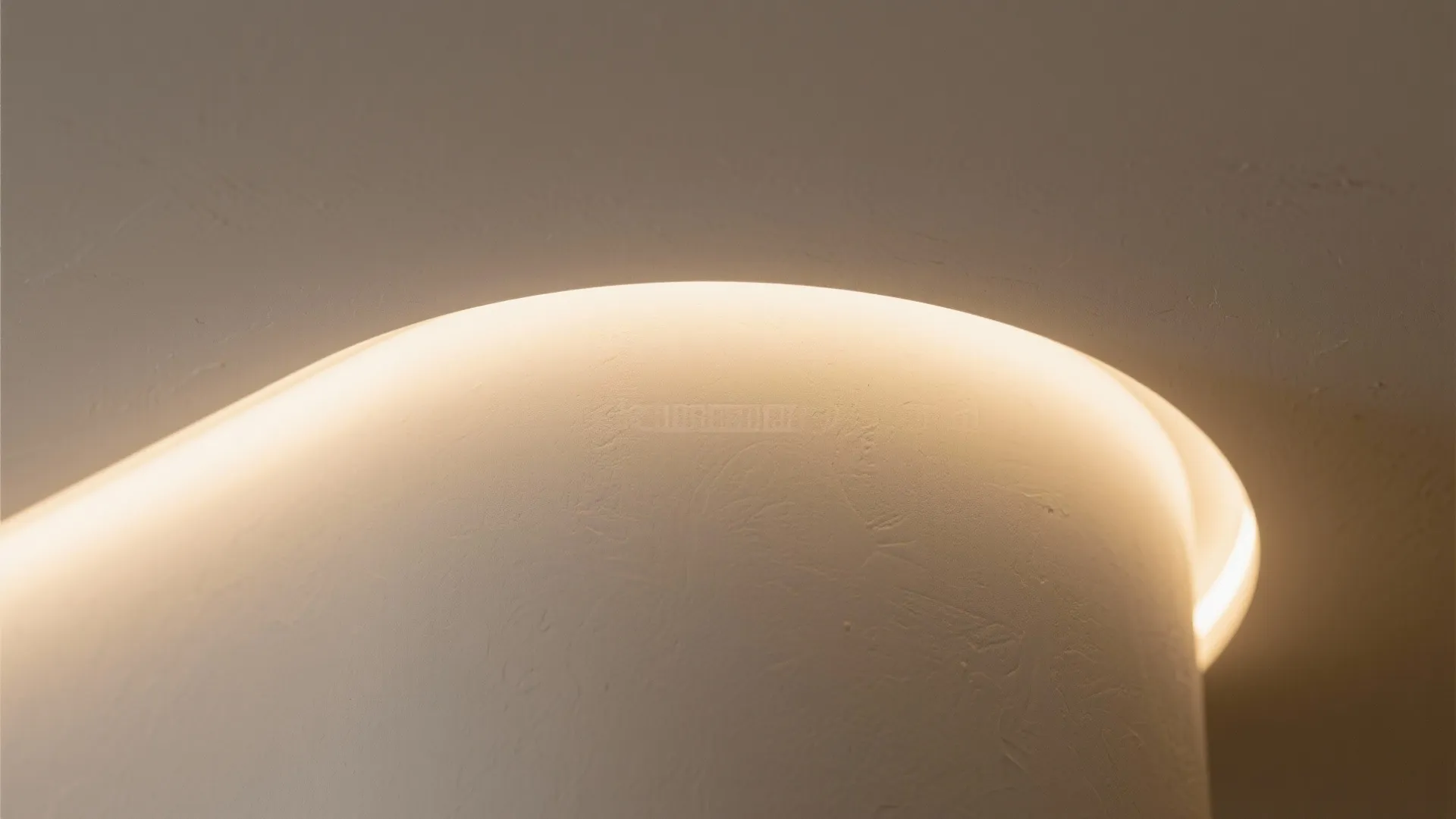 Close up view of a curved wall featuring warm hidden lighting and smooth white surface