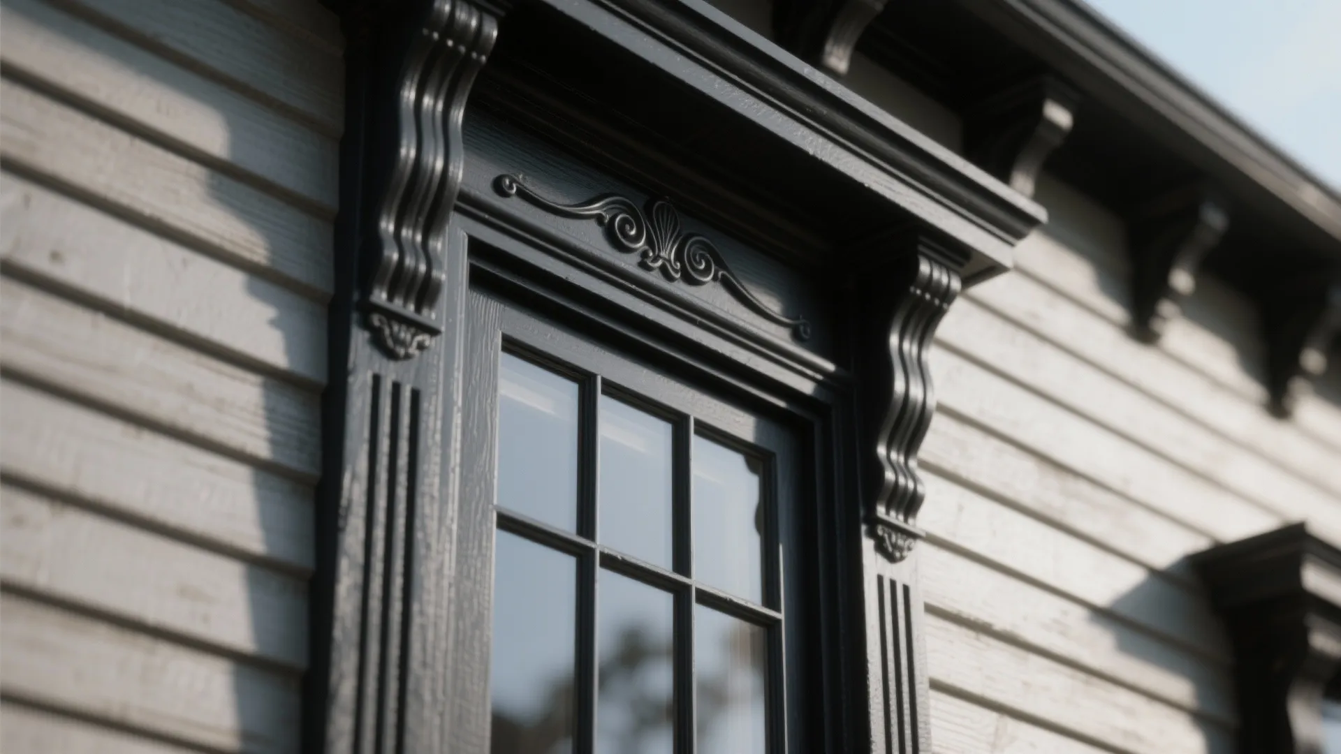 Close up of a window with dark decorative trim and moldings on light gray house siding