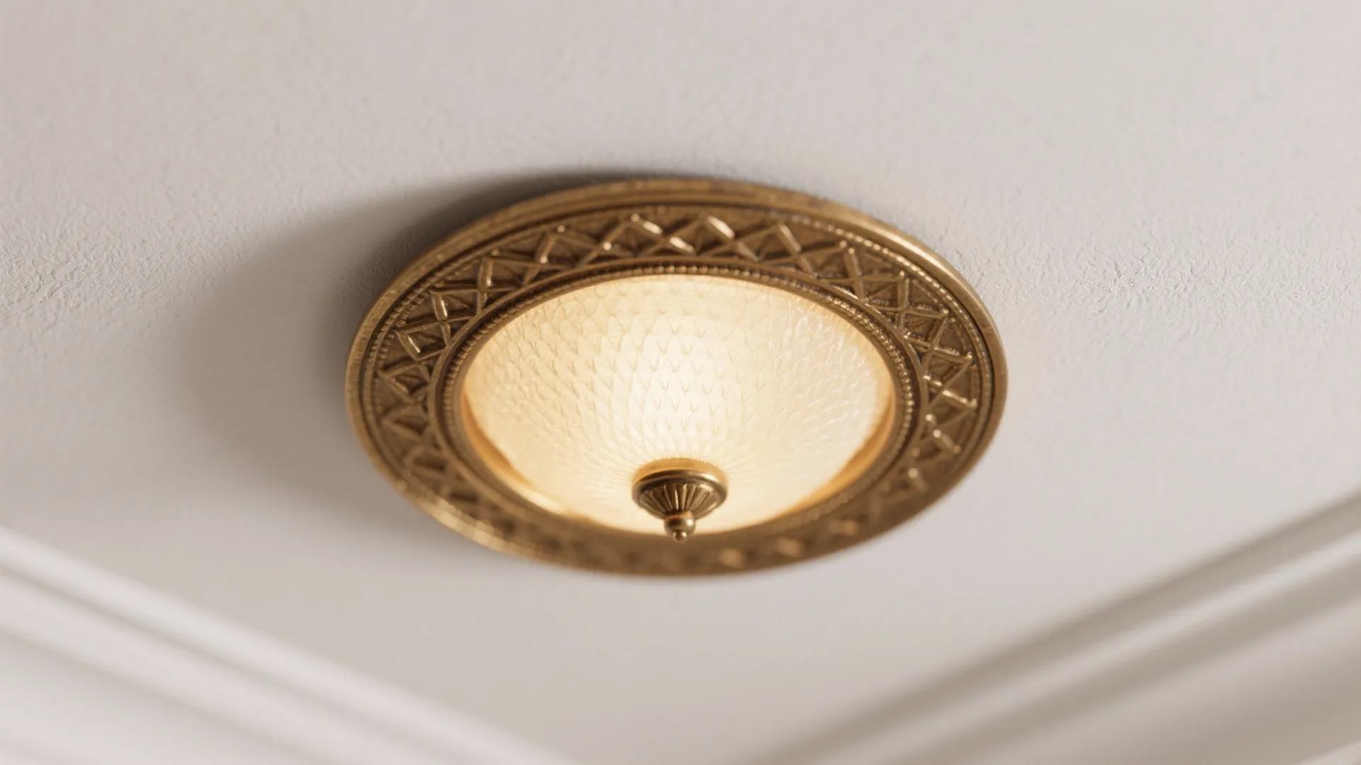 Classic gold ceiling light fixture with detailed pattern and warm glow on a white flat ceiling