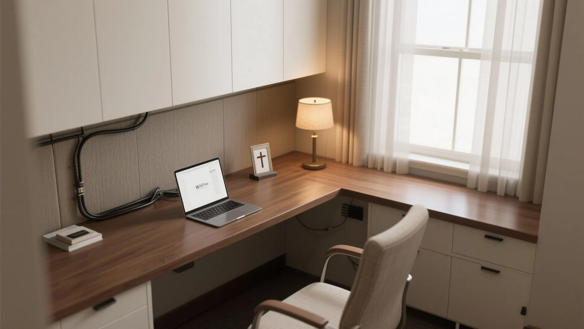 Small workspace with a wooden corner desk, laptop, desk lamp, white cabinets, and window curtains