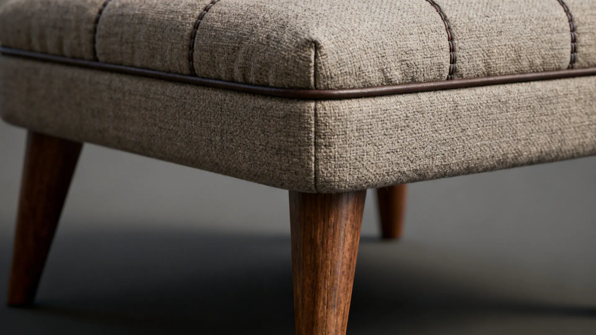 Close-up of ottoman stitching, wood leg joinery, and performance fabric texture.