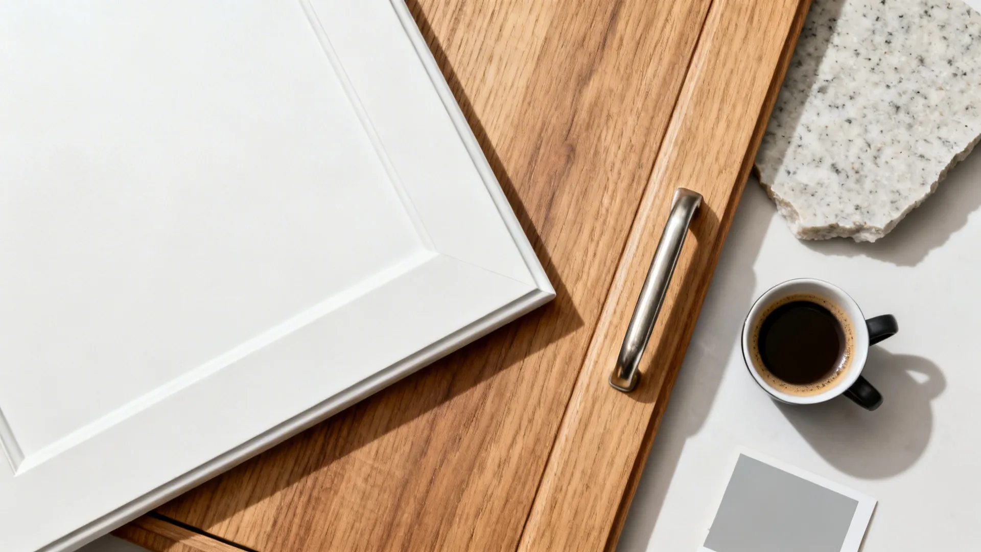 Flat lay of matte white door sample, oak veneer, nickel handle, and quartz chip for a diagonal corner cabinet.
