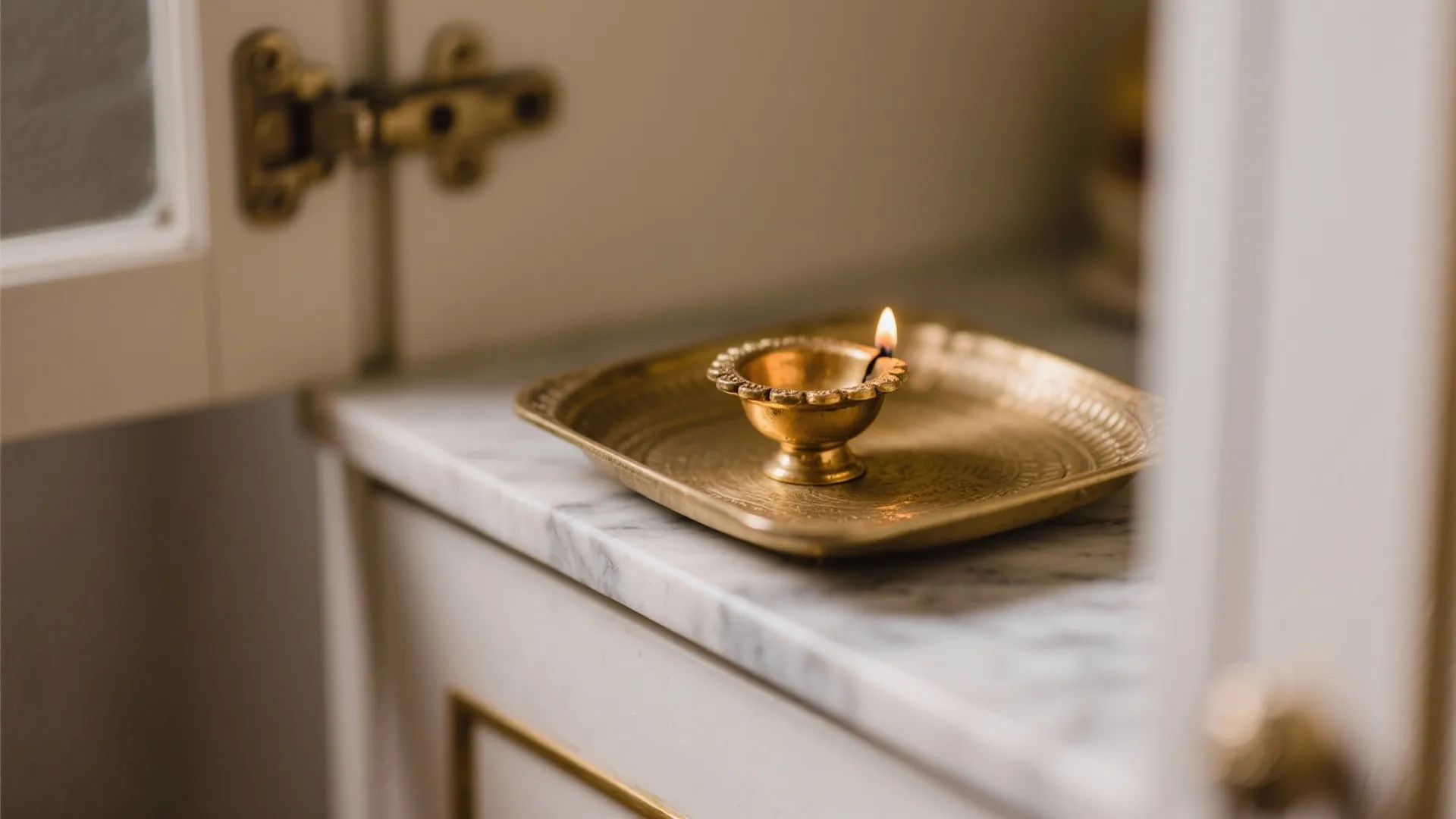 Small gold oil lamp with flame on brass tray placed on marble surface of cabinet