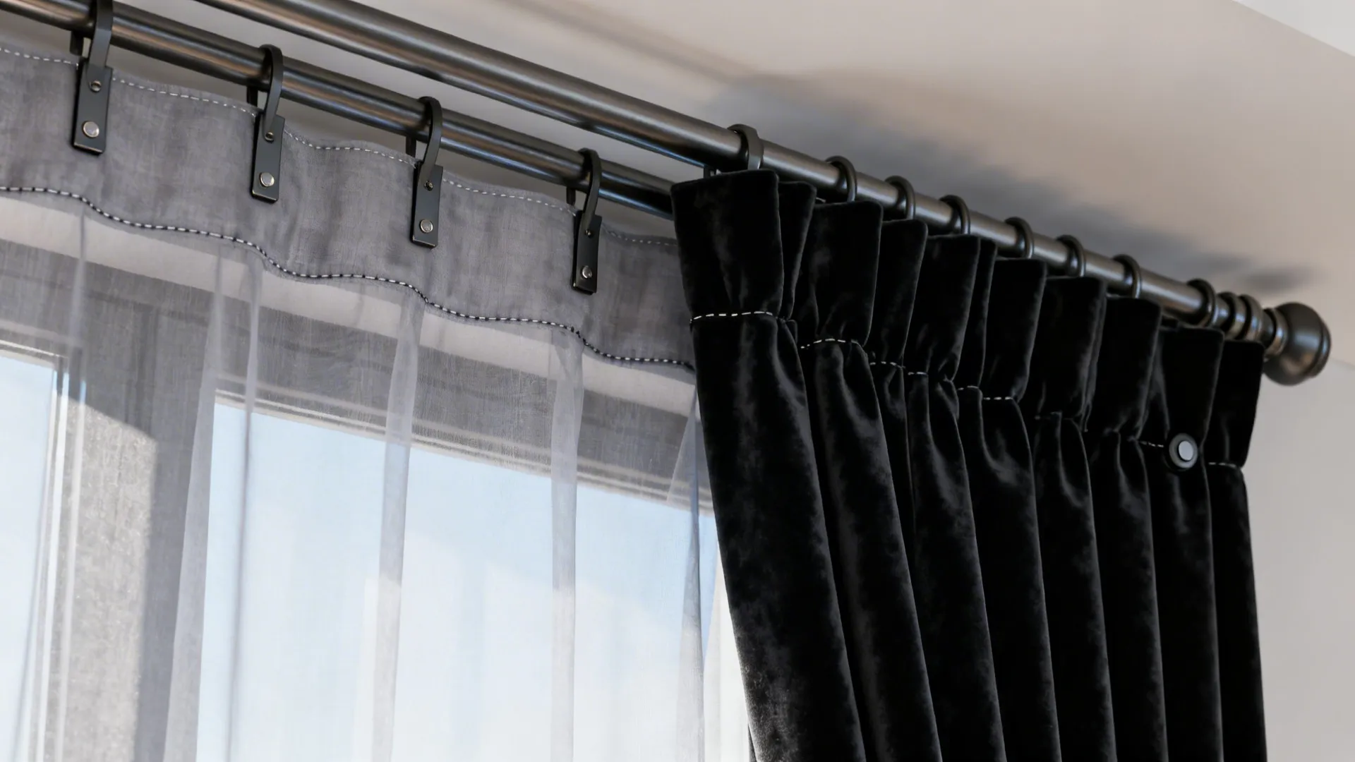 Double metal curtain rod holding sheer grey fabric and thick black velvet curtains by window