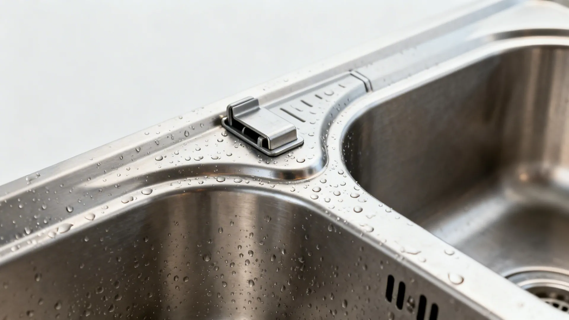 Macro detail of stainless double-bowl sink rim and clip-on drainboard mechanism.