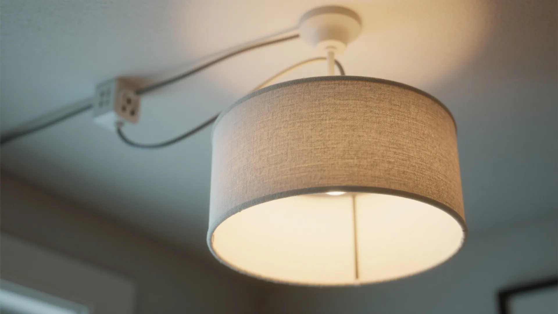 Fabric drum shade ceiling light with visible wiring connected to a power outlet on ceiling