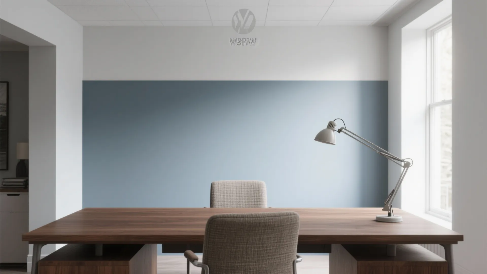 Wooden office desk with grey chair and desk lamp against a blue and white wall