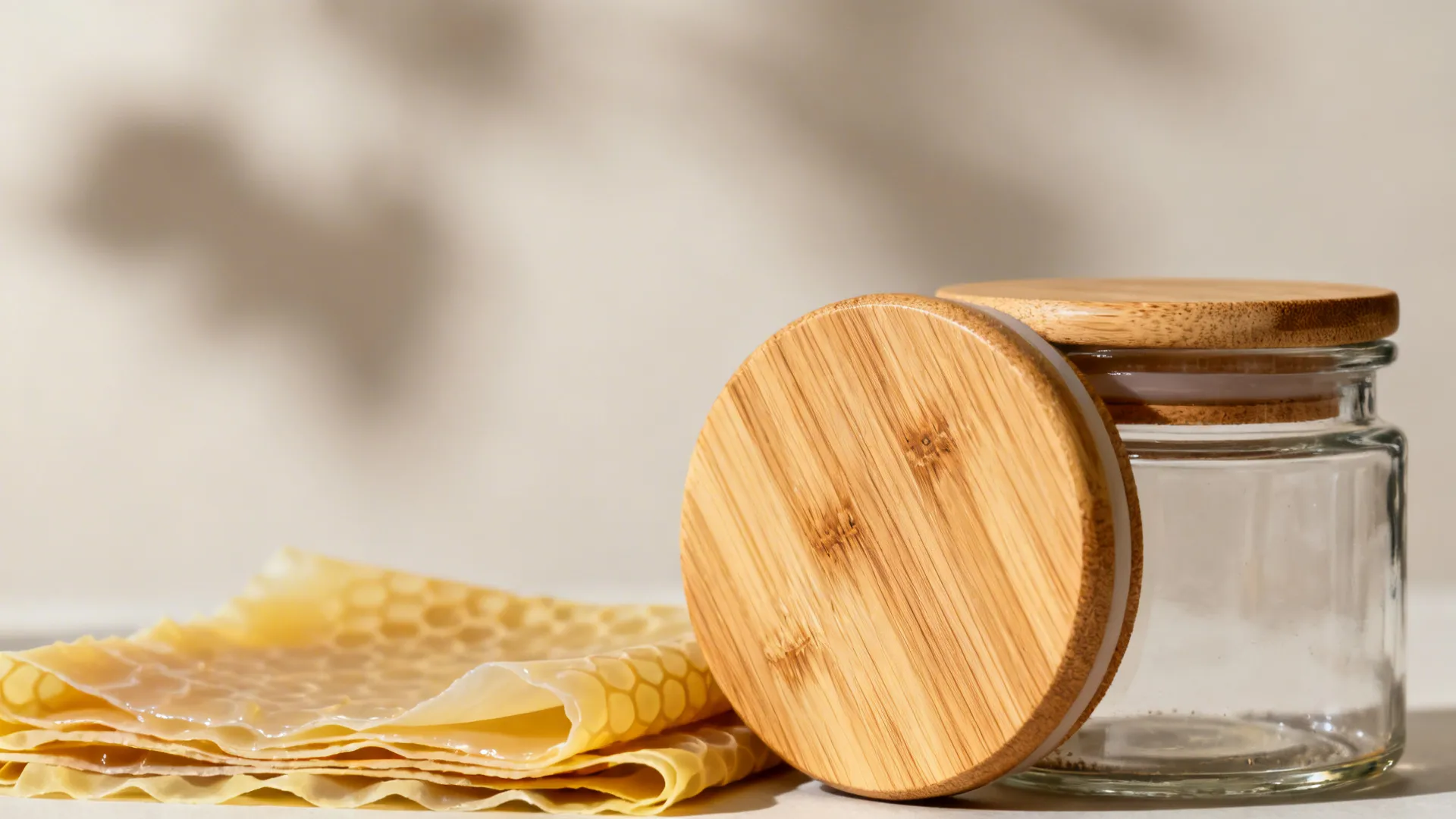 Close-up of empty glass jar with wooden lid leaning against it next to beeswax wraps