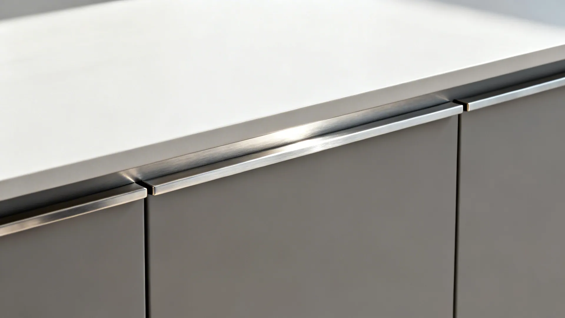 Close-up of brushed stainless edge pull wrapping the top of a matte cabinet door.