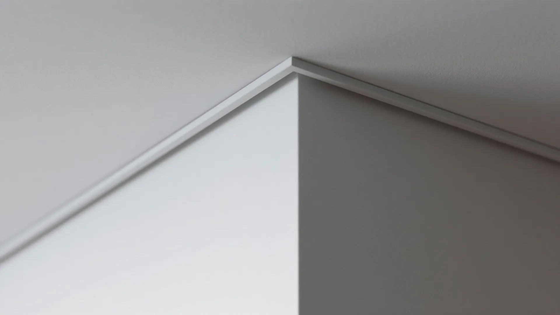 Close-up view showing clean white wall corner with a shadow gap line and ceiling connection