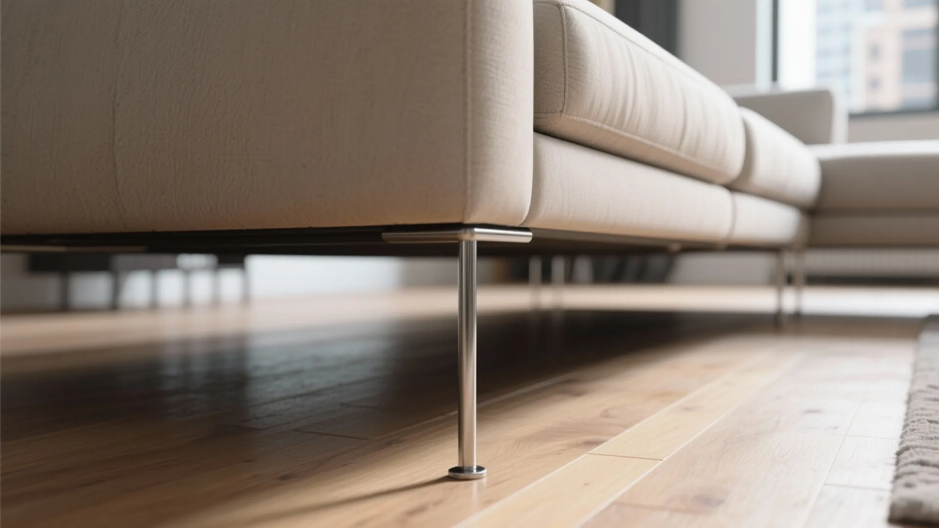Close up of thin metal legs on a modern beige sofa over light wood floor