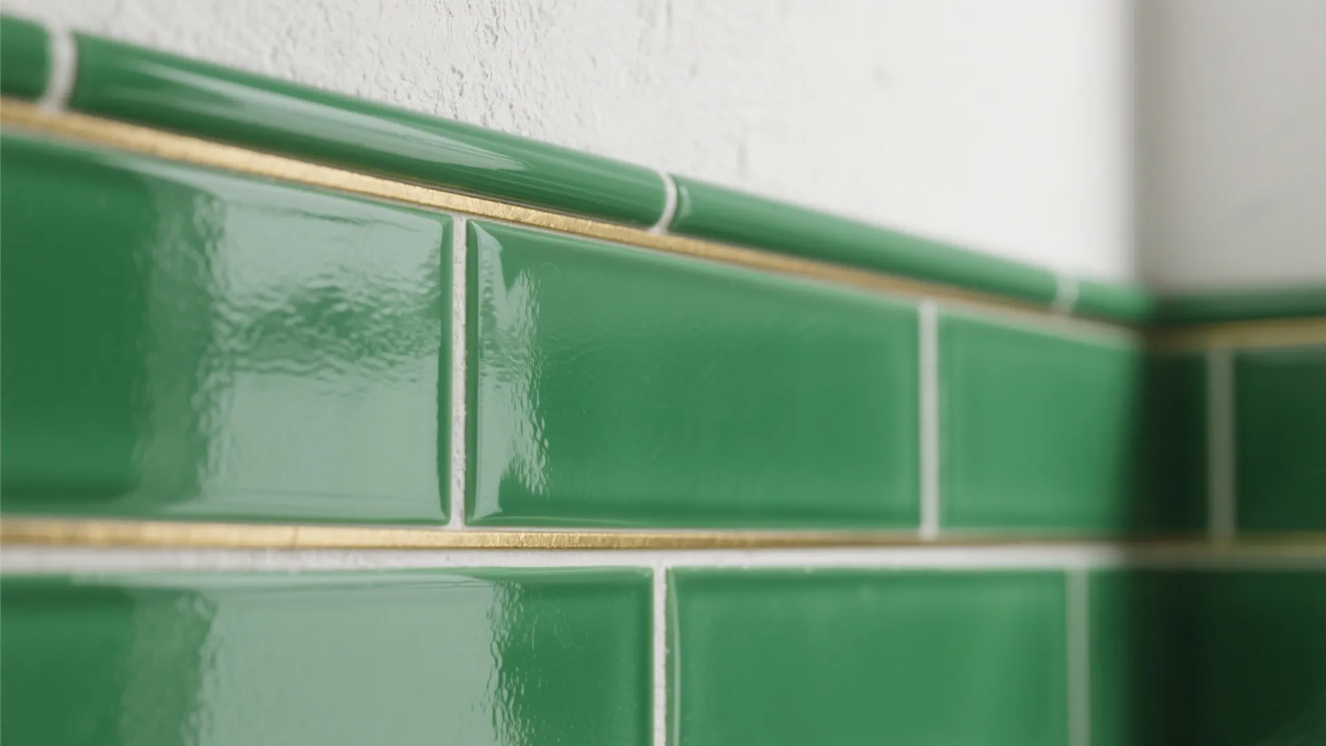 Brass trim between emerald subway tile and white plaster, close-up of grout and texture