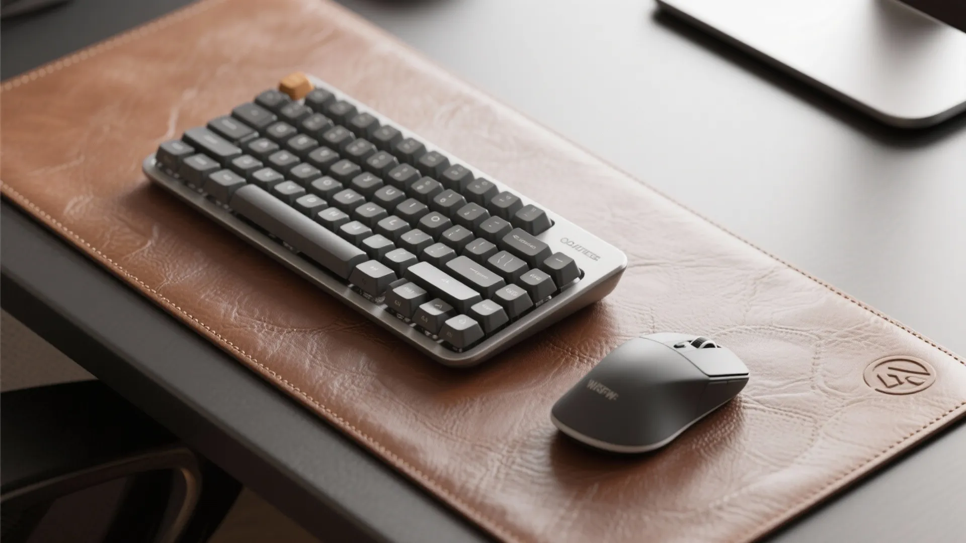 Grey keyboard and mouse on brown leather desk mat placed on a dark colored office desk