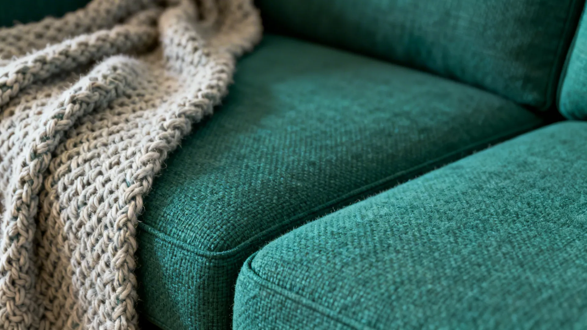 Macro view of emerald sofa fabric and knitted throw showing texture and weave.